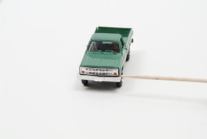 A toothpick appears to apply reddish fluid to a green pick-up truck's turn signal
