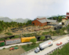 A diesel-locomotive-led Santa Fe train passes under a highway with a lumber mill in the background.