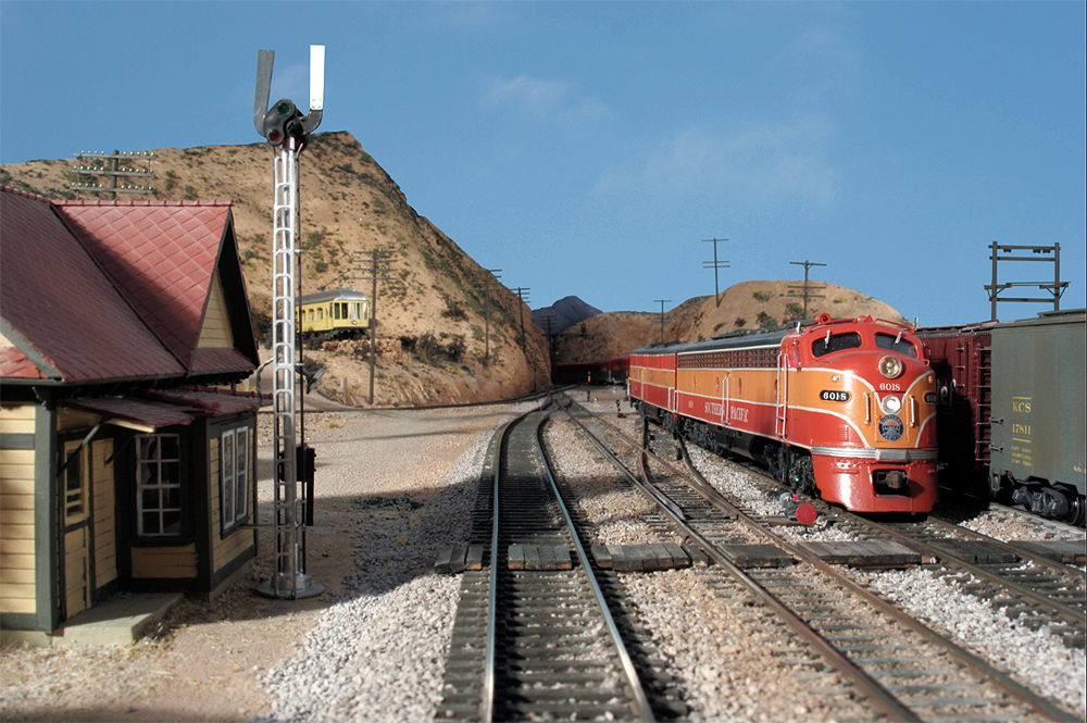 A two-one orange Southern Pacific passenger train glides through a high-desert southern California scene depicting Cajon Pass.