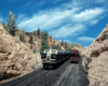 A blue-and-yellow Santa Fe diesel locomotive leads a train through an HO Scale stone walled gorge.