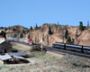 Red-and-silver Santa Fe passenger locomotives pull a train to meet with a blue-and-yellow Santa Fe freight locomotive-hauled train in an arid scene in front of a livestock loading area.