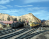 A Union Pacific train nears the top of the grade in an arid scene at "Summit" in Cajon Pass while a Santa Fe steam locomotive idles near the dispatcher's station.