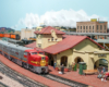 A red-and-silver Santa Fe diesel locomotive leads a train paused at a southern California city.