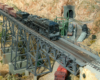 In the arid mountains along the Santa Fe rights-of-way, a Southern Pacific cab-forward steam locomotives operates on a trestle over a short Santa Fe diesel-powered freight train.