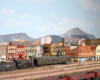 A small consolidation-type locomotive pushes a diner to a bumper post next to a Santa Fe depot in a yard with at least six parallel tracks.