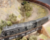 A heavy-duty steam-locomotive, likely a 2-10-4 hauls a train upgrade over a bridge on a Santa Fe-themed layout.