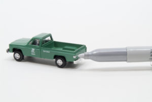 A silver felt tip marker is held near the rear of a green HO scale pick-up truck on which the marker colored taillights.