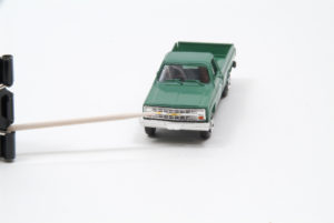: A toothpick held by a alligator paper clip points to where yellow fluid colors an emblem on a green pick-up truck's grill.