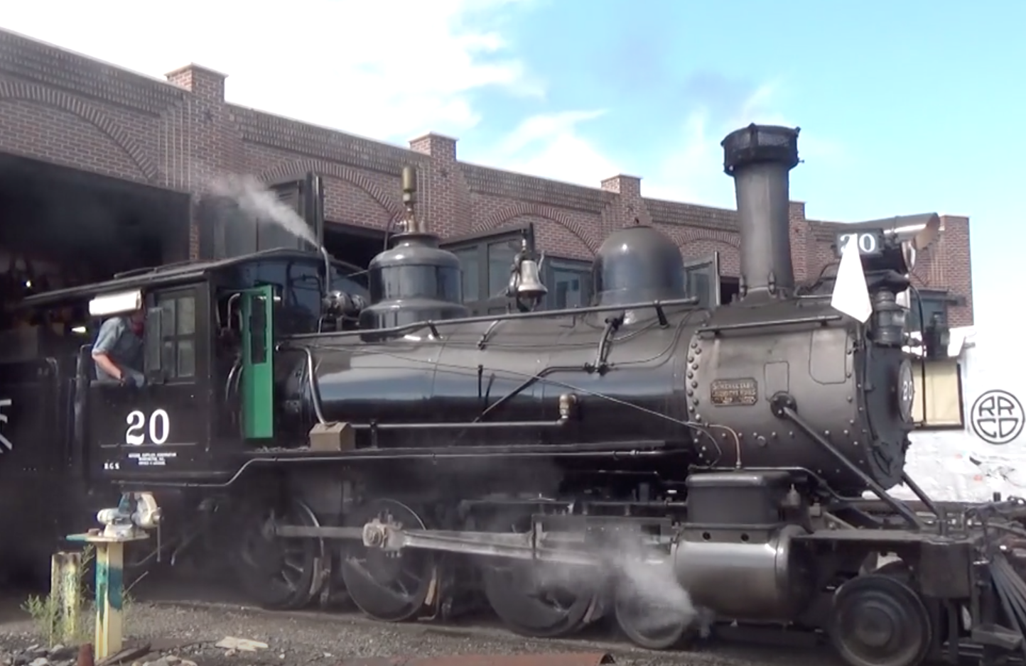 Steam locomotive moves out of a roundhouse.