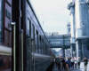 A woman walks toward a camera alongside a train stopped a station.