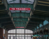 Green painted steel arches and a glass ceiling focused on  "To Trains" sign.