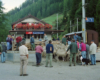 A crowd of people surround a herd of sheep at a makeshift enclosure next to a train station.