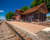 A one-story brick passenger train station appears in sunlight under clear skies in summertime.