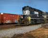 A railroad worker rides the steps of a black diesel locomotive in a yard.