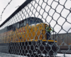 Yellow diesel locomotive behind a chain link fence on a cloudy day.