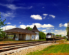 An Amtrak passenger train passes by an old and falling down train station.