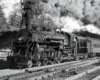 A steam locomotive hauling a passenger car on a multi-track mainline.