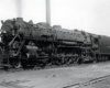 A large steam locomotives pauses in a rail yard.