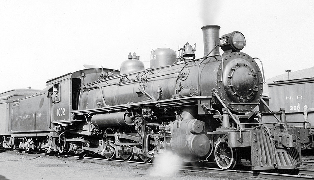 A steam locomotive at the head of a train releasing steam in a rail yard.