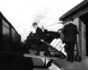 Uniformed railroad worker pulls a loaded dolly up a ramp to an express car.