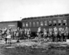 Soldiers in loose formation wearing what appears to be winter clothing in front of a mixed train.