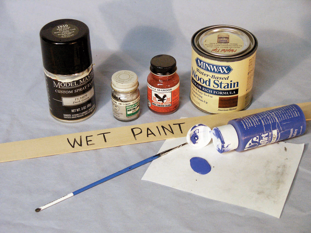 Assortment of paints plus a paint stir stick labeled “wet paint.”