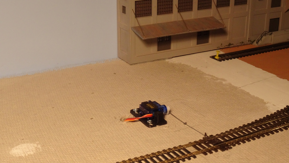 ALT: A small servo is connected by a stiff wire to the model railroad turnout it controls.