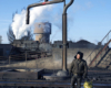 A man stands near a water standpipe in a rail yard.