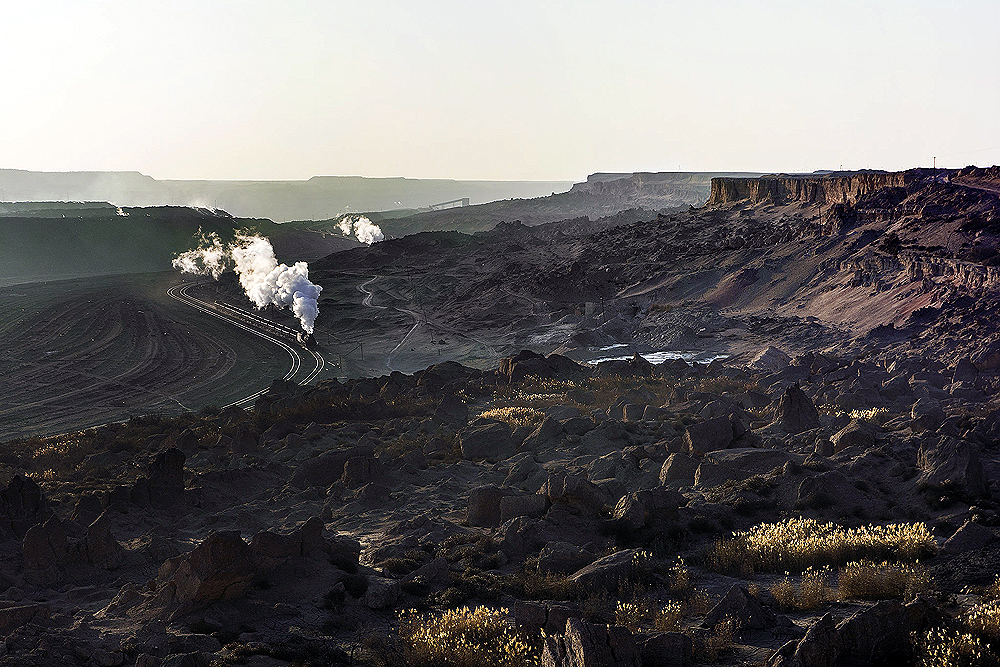 A distant train winds through a curve below cliffs and rocks.