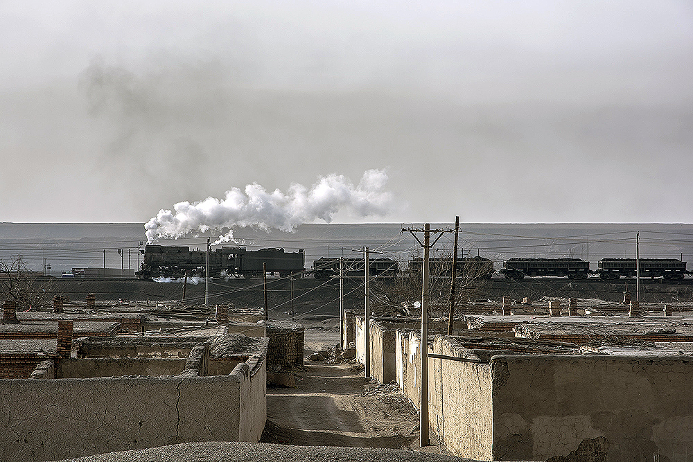 Steam locomotive hauling a train in the background behind a ruined neighborhood.
