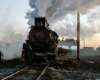 A steam locomotive pauses with a train in an industrial rail yard.