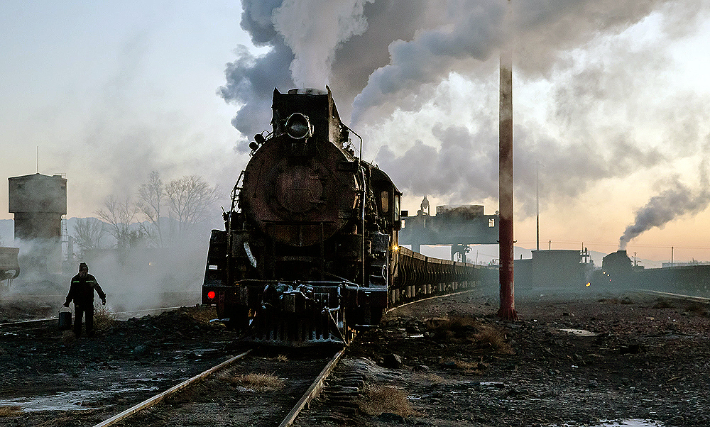 Steam locomotive paused in an industrial rail yard.