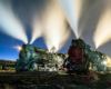 Two steam locomotives emitting steam on a star-lit night in a rail yard.