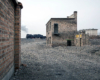 A steam locomotive passes in the background between abandoned buildings.