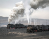 Two steam locomotives appear in the bottom of an open pit coal mine waiting for loads.