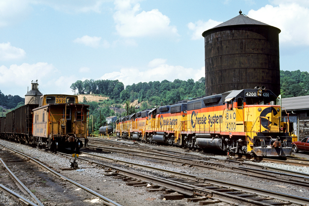 Yellow, blue, orange painted "Chessie" locomotives and a caboose appear in a rail yard.