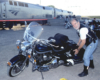 Man posing with motorcycle near a passenger train.