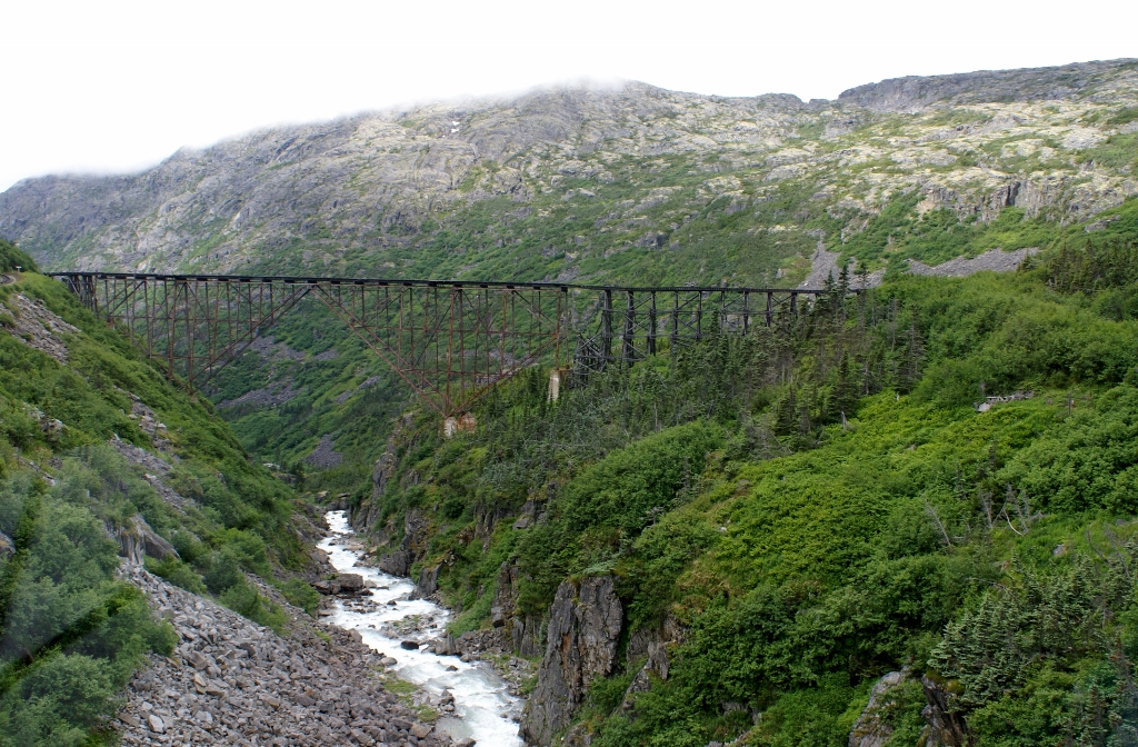 Decrepit wood and steel bridge perched over frothy mountain stream.