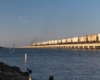 Locomotives hauling a hopper train over a long causeway over a body of water.