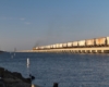 Locomotives hauling a hopper train over a long causeway over a body of water.