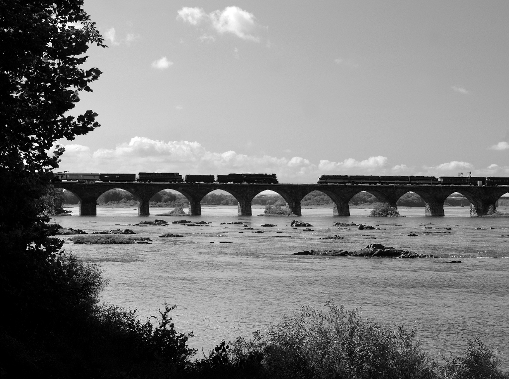 Black and white image of two trains paused on a bridge.