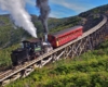 A geared funicular steam locomotive pushing a passenger car up a steep-inclined trestle.