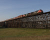 Black and red locomotives hauling a mixed train over a long wood trestle.