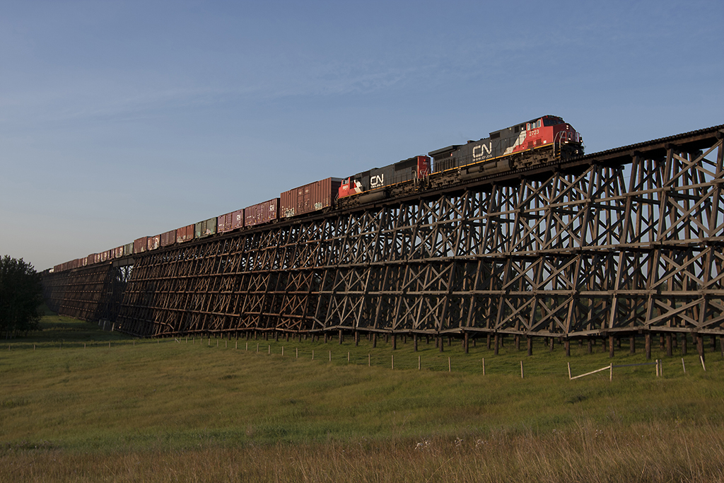 Black and red locomotives hauling a mixed train over a long wood trestle.