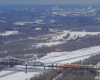 Overhead view of a train moving across a bridge above a frozen river in winter time.