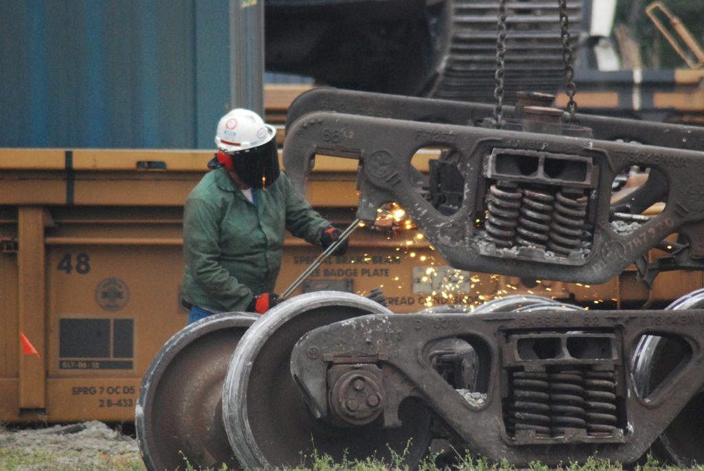 Railroad worker with torch creating sparks with a freight car truck.
