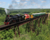 Steam locomotive hauling a mixed tourist train over a long bridge.