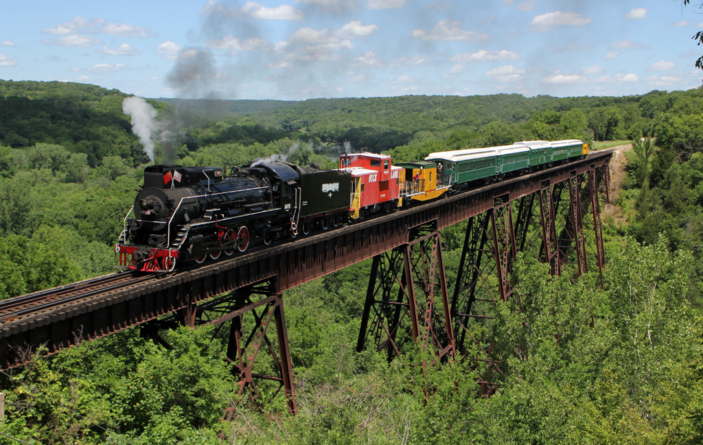 Steam locomotive hauling a mixed tourist train over a long bridge.