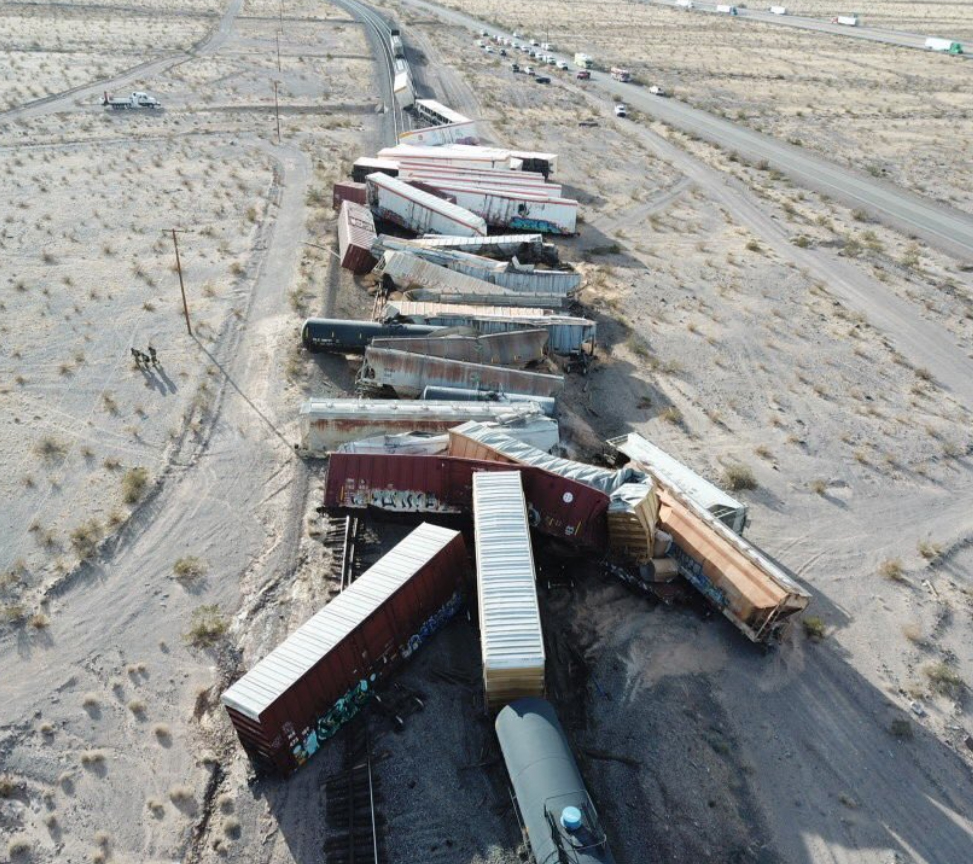 A vertical image of a train derailment in an arid landscape with low-angle sunlight.