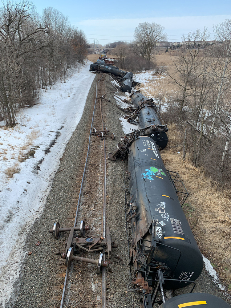 Derailed tank cars along single track main line in snowy rural scene.